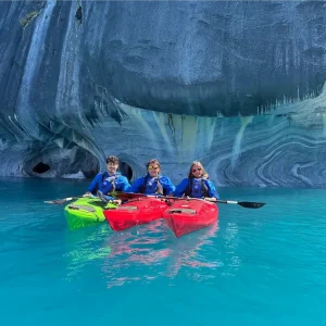 Personas en kayak frente a las Catedrales de Mármol en el Lago General Carrera, sobre aguas turquesas y roca veteada.
